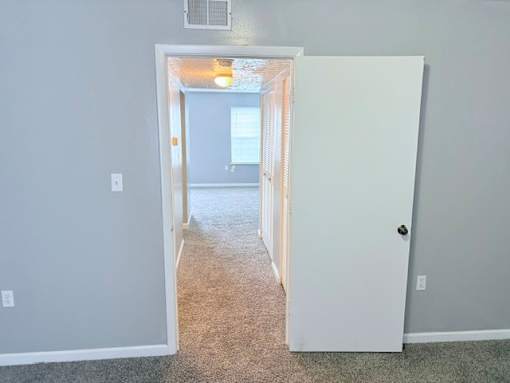 A white door is open to a hallway with a carpeted floor.