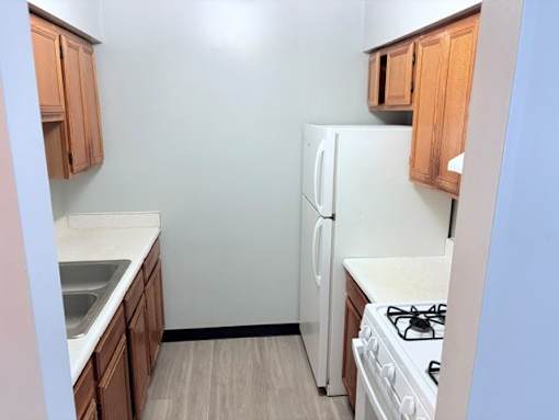 A kitchen with a white refrigerator, wooden cabinets, and a white stove top.