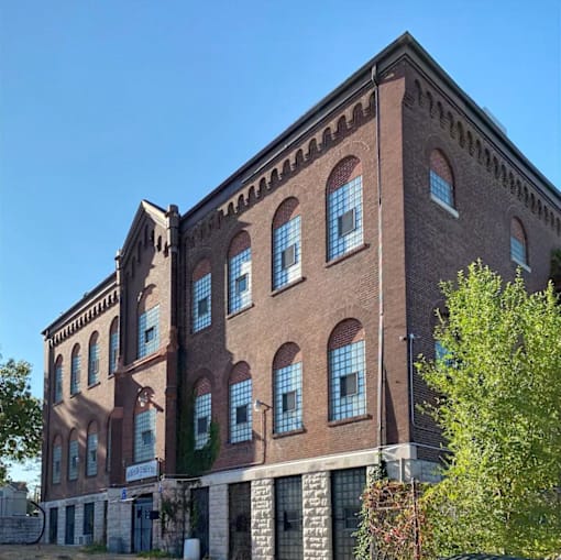 A large red brick building with many windows and a tree in front.