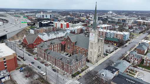 A church with a tall steeple is in the middle of a city intersection.