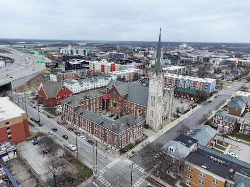 A church with a tall steeple is in the middle of a city intersection.