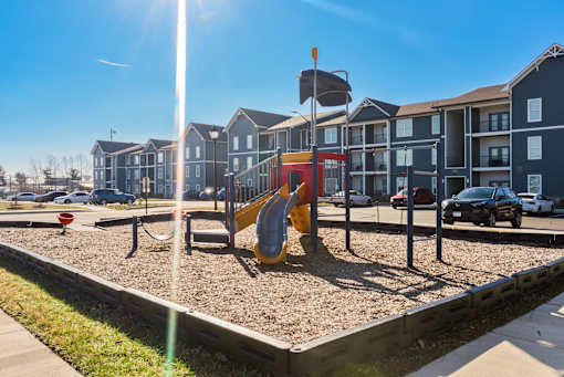 A playground with a yellow slide in front of apartment buildings.