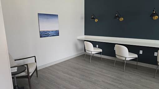 A room with a grey floor, a white chair, a black chair and a painting on the wall.