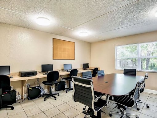 A conference room with a table surrounded by chairs and computers on desks.