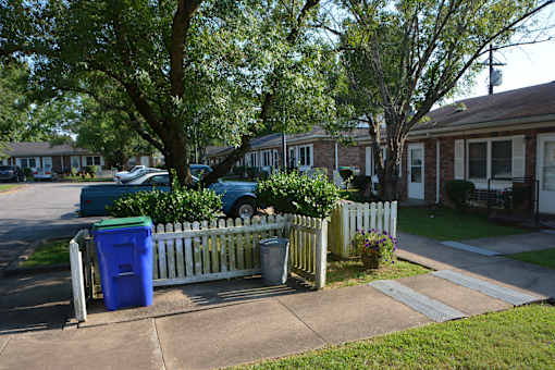 a white fence in front of a house with a blue trash can