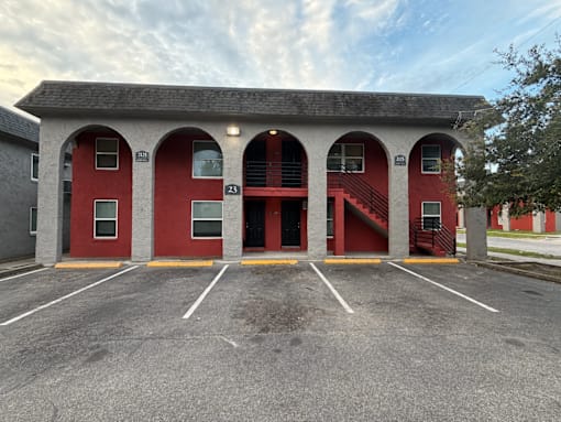 A red building with arched windows and doors is surrounded by a parking lot.
