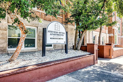 A sign for Stevens-Duval Apartments stands in front of a brick building.