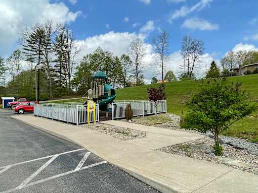A playground with a green slide and a red car parked in the background.