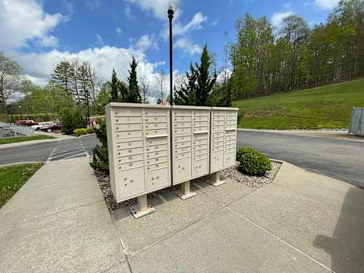 A large, beige, metal mailbox with multiple compartments is situated on a concrete sidewalk.