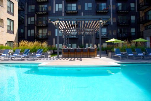 a large pool with chairs and a wooden structure in front of a building