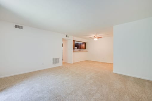 an empty living room with white walls and carpeting and a ceiling fan