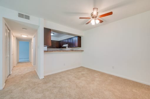 a empty living room with a ceiling fan and a kitchen