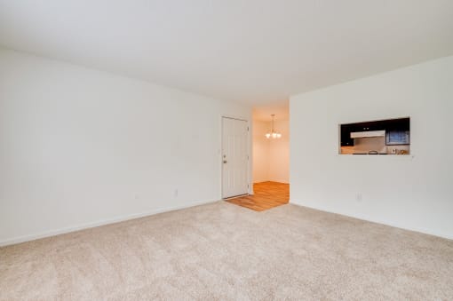 a spacious living room with carpet and a door to a kitchen