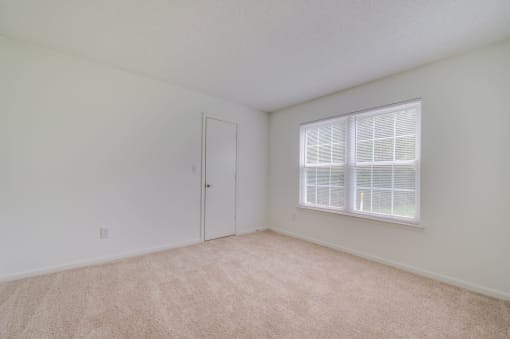 a spacious bedroom with a large window and carpeting