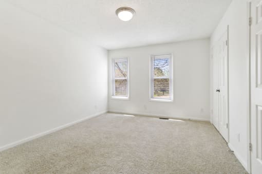 an empty room with two windows and a carpeted floor