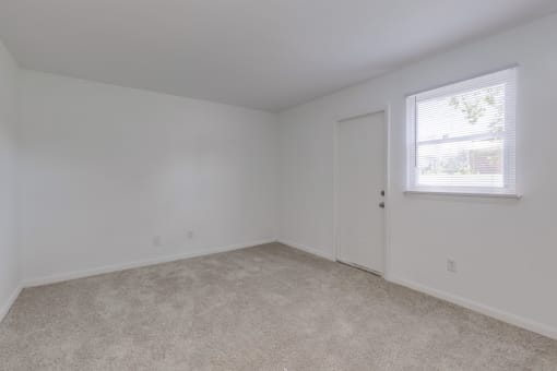 a bedroom with white walls and carpet and a window