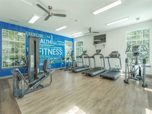 a gym with cardio equipment and weights in a room with windows