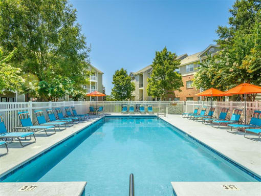 a swimming pool with blue chairs and orange umbrellas in front of a building