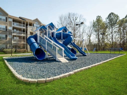a playground with a blue playset in front of an apartment building