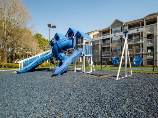 a playground with a blue slide and swings in front of an apartment building