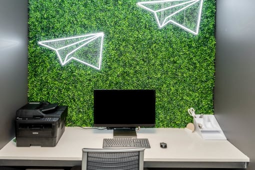 a desk with a computer and a chair in front of a wall covered in green plants