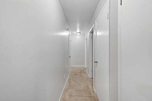 A long hallway with white walls and carpeted flooring.