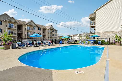 A swimming pool surrounded by chairs and umbrellas in front of apartment buildings.