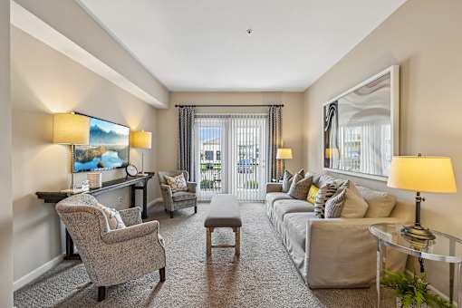 A well-lit, spacious living room with a grey sofa, a grey armchair, a grey coffee table, and a painting on the wall.