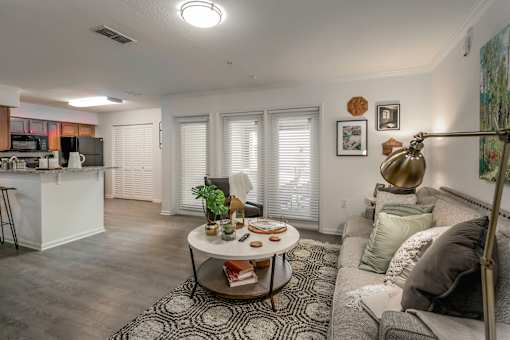A modern living room with a grey sofa, a coffee table, and a kitchen area in the background.