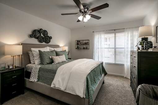 A bedroom with a bed, dresser, and ceiling fan.