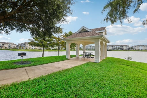 a gazebo with a picnic table on the grass next to the water