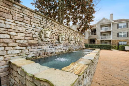 a stone wall with a fountain in front of a house at 10X Audubon Park apartments in Daphne, AL 