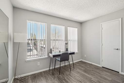 A room with a desk and chair in front of a window with blinds.