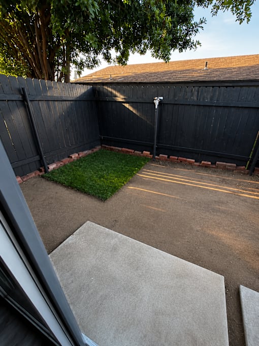 A backyard with a black fence and a concrete patio.