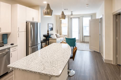 Open kitchen island with living area and pendant lighting at Avion at West Lemmon Apartments, Dallas