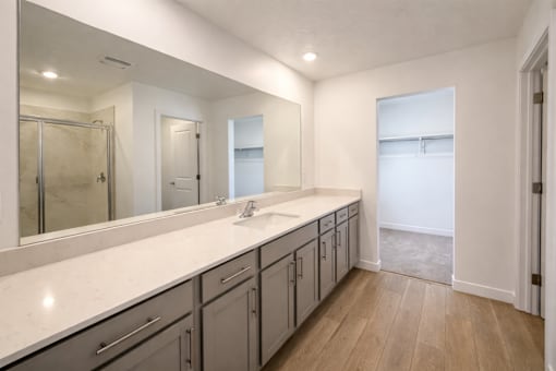A bathroom with a large mirror, sink, and cabinets.