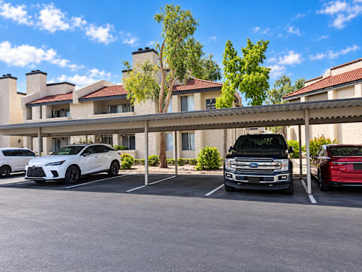 Covered parking with residential buildings and trees at Gentrys Walk Apartments, Mesa, Arizona