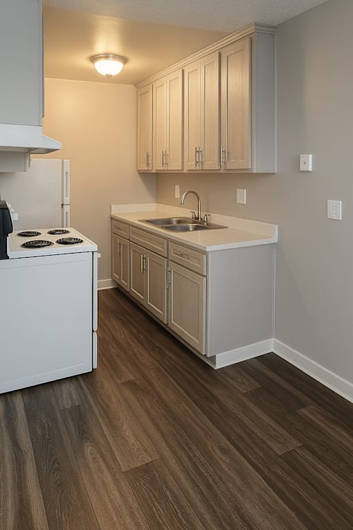A kitchen with a white stove top oven and a white sink with a white counter top.