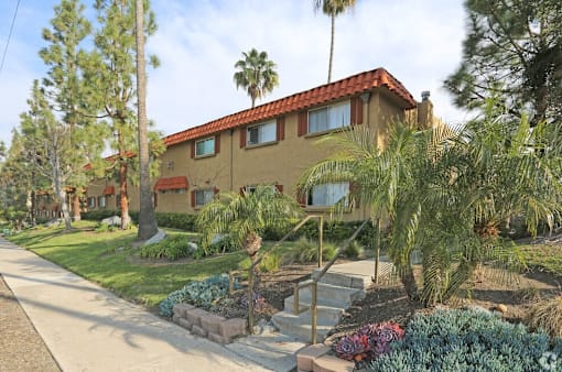 A house with a red tile roof is surrounded by green plants and trees.