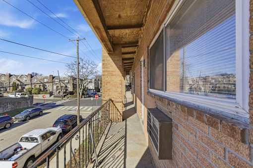 A balcony with a brick wall and a window overlooking a street with cars and houses.