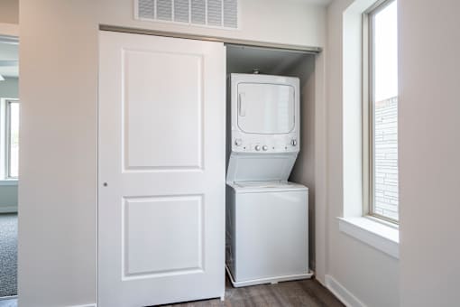 A white door is open to a small room with a white washing machine in it.