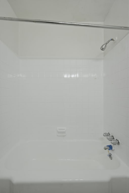 A white bathroom with a white tub and a shower head.