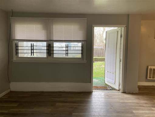 A room with a window covered by white blinds and a door open to a backyard.