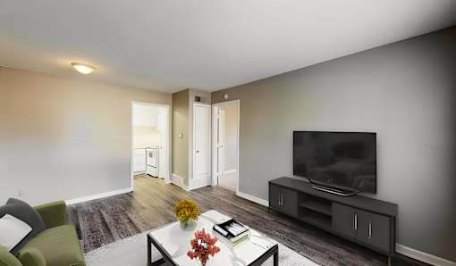 A living room with a green chair, a coffee table with a vase of flowers, and a television on a cabinet.