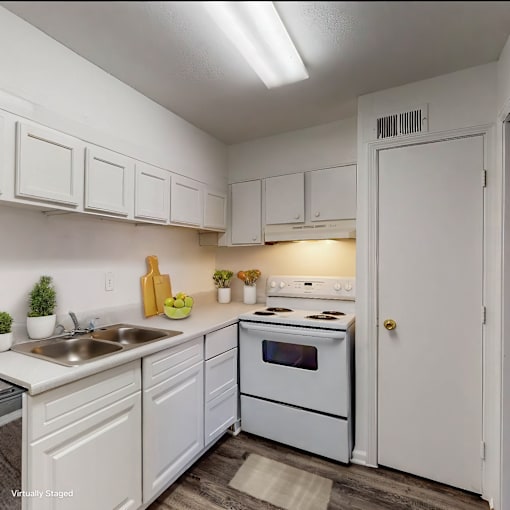 A white kitchen with a sink, stove, and cabinets.