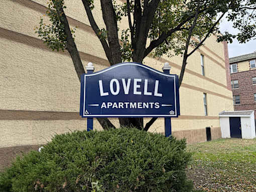 A blue sign that says Lovell Apartments stands in front of a building.