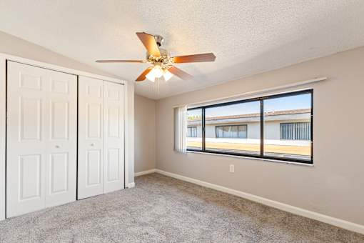 A room with a ceiling fan and a window overlooking a building.