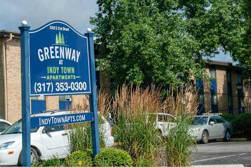 A sign for Greenway at Indy Town Apartments stands in front of a parking lot.