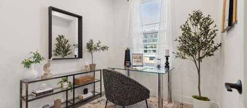 A black chair sits in front of a glass table with a mirror above it.