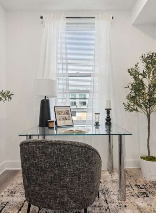 A grey chair sits in front of a glass table with a laptop on it.